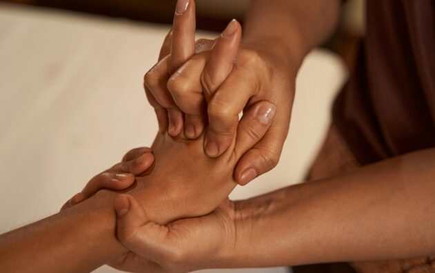 Massotherapist stretching patient digits during Thai massage session