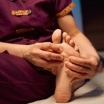 Qualified massotherapist giving Thai foot massage to female client