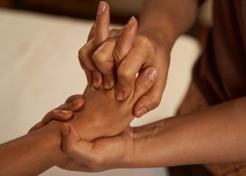 Massotherapist stretching patient digits during Thai massage session